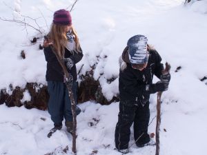 To skolebørn undersøger sne, is og vand i en bæk.