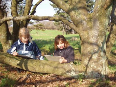To piger skriver postkort ved et træ i skoven.